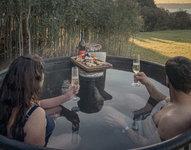Pareja-en-tinaja-caliente-con-champagne-tabla-y-atardecer-dorado